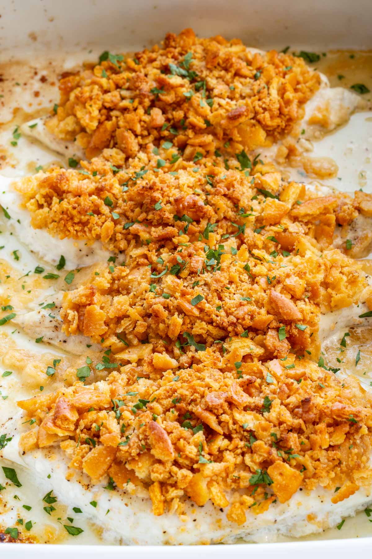 Angled close-up of baked fish fillets in a white dish showing the texture of the crispy, golden-orange Ritz cracker topping scattered with fresh parsley.