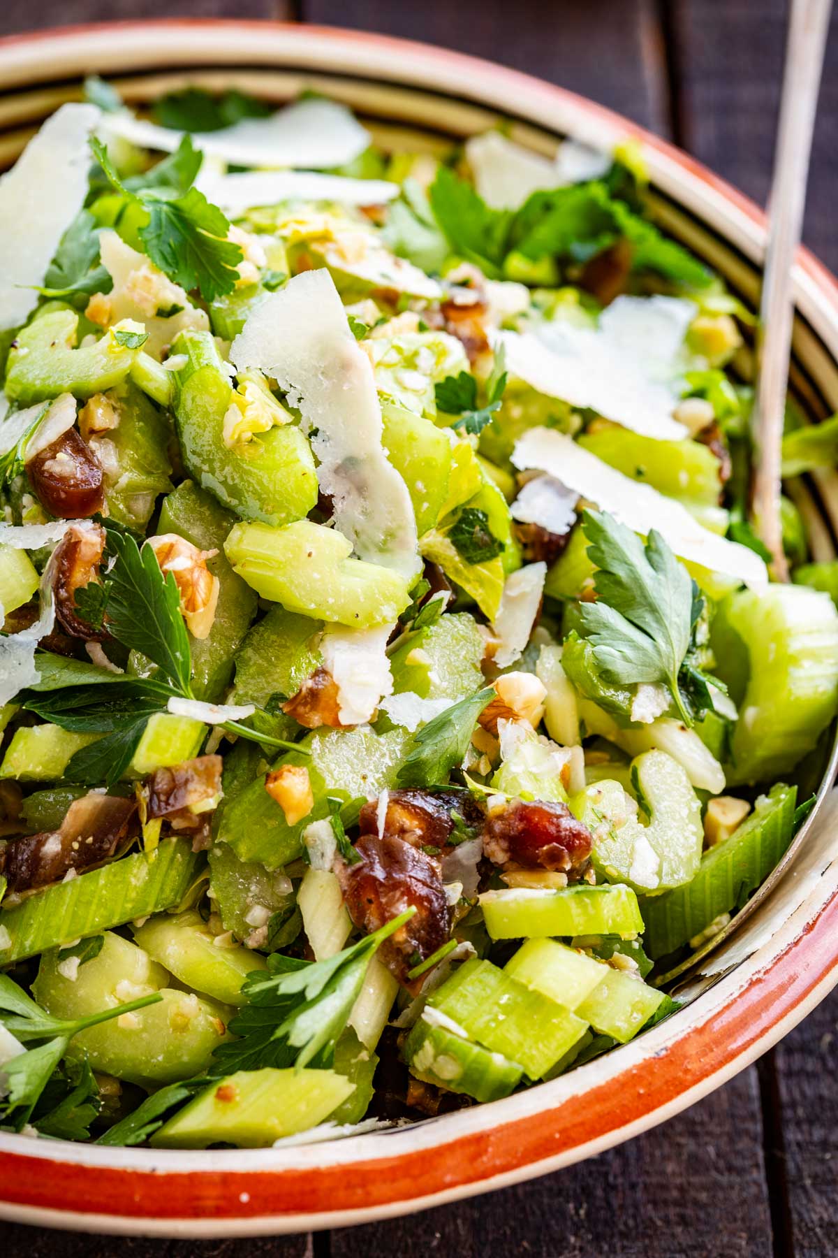 Very close macro shot of the celery salad, highlighting the texture of sliced celery stalks, whole parsley leaves, chopped walnuts, caramelized date pieces, and thin Parmesan shards.