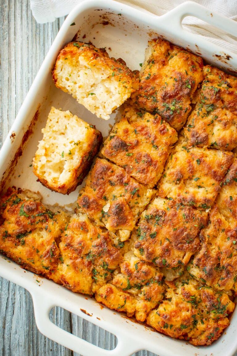 Overhead view of cheddar bay butter swim biscuits in a white baking dish, with one biscuit broken in half to reveal a soft, pillowy crumb.