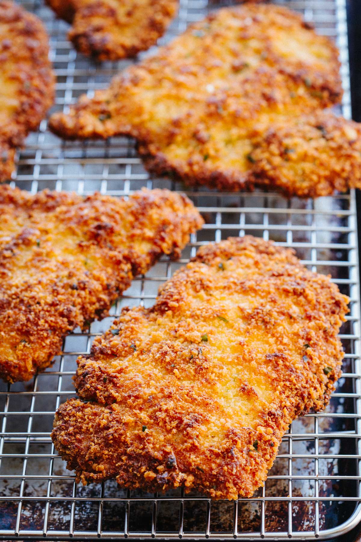 Tight close-up of golden, crunchy pan-fried veal cutlets stacked on a wire cooling rack, highlighting the crisp, uneven breadcrumb coating.