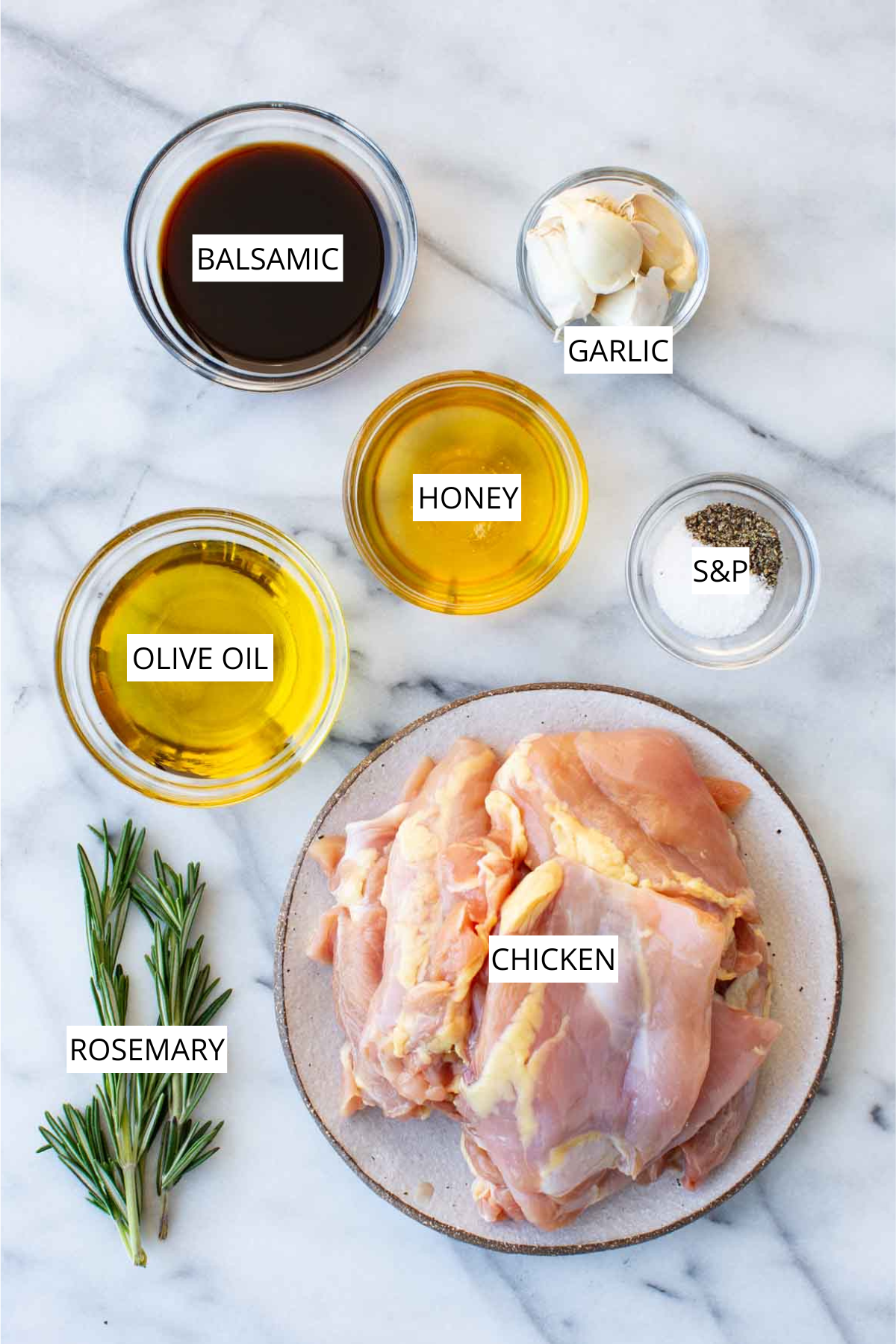 Overhead flat lay of honey balsamic grilled chicken ingredients on a white marble surface: a glass bowl of dark balsamic vinegar, a small bowl of garlic cloves, a bowl of golden honey, a small dish of salt and pepper, a large bowl of olive oil, fresh rosemary sprigs, and a plate of raw bone-in, skin-on chicken thighs, each ingredient labeled in white text.