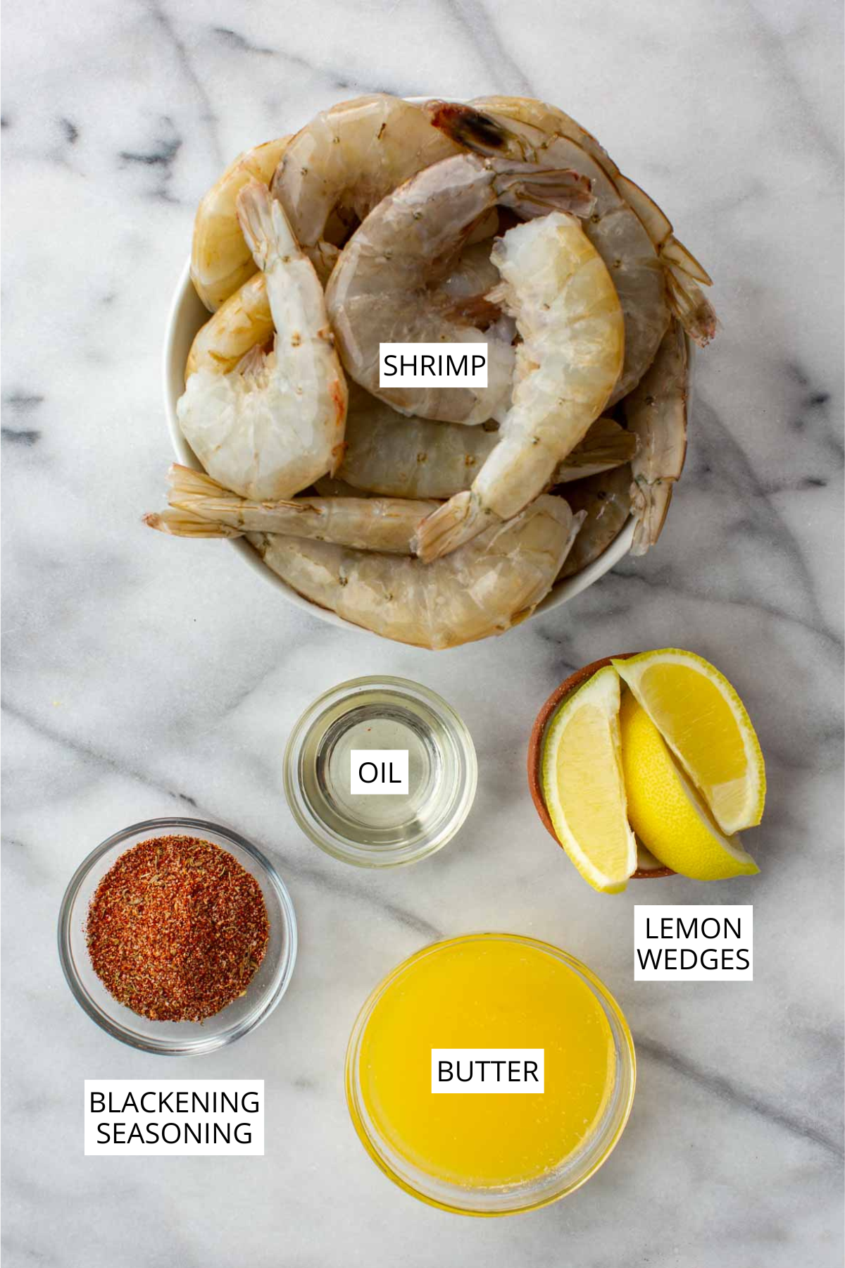 Overhead shot of ingredients including shrimp, blackening seasoning, lemon wedges, oil and butter.