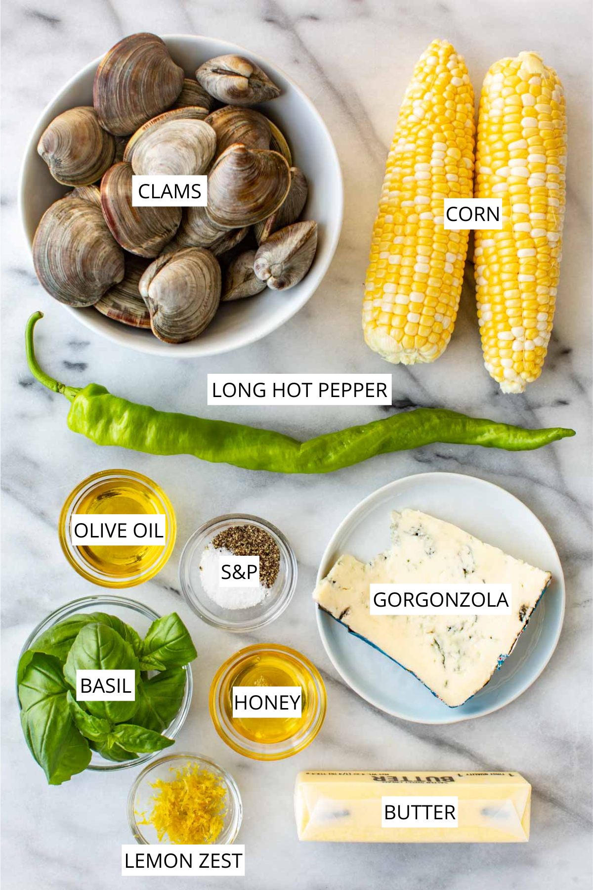 Flat lay of ingredients on a white marble surface, labeled: clams in a white bowl, two ears of corn, a long hot pepper, olive oil, salt and pepper, gorgonzola cheese, fresh basil, honey, lemon zest, and butter.
