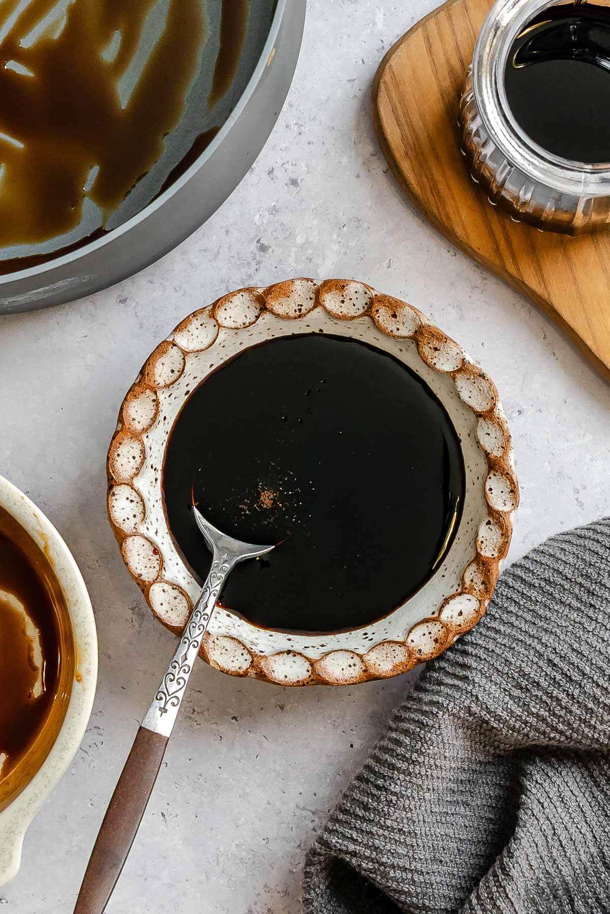 Overhead shot showing a ceramic plate full of balsamic reduction next to a sauce pan and kitchen towel.