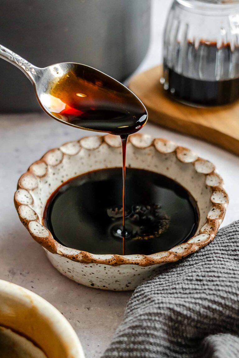 Thick balsamic reduction being poured off a spoon over a small bowl next to a kitchen towel.