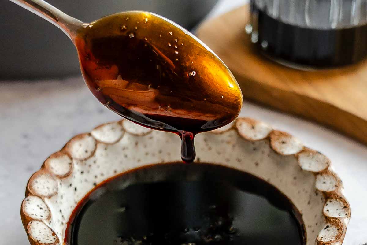 Syrupy balsamic reduction being poured with a tablespoon.