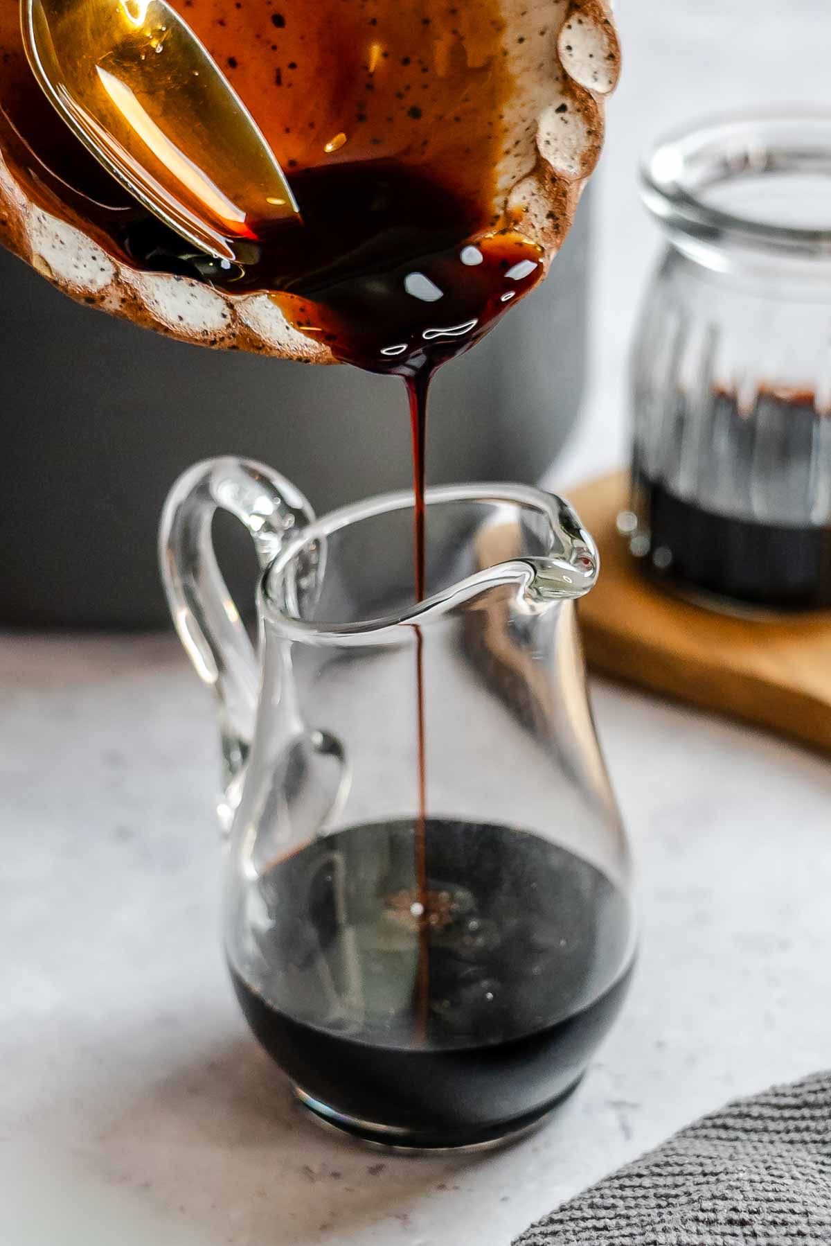 Syrupy balsamic reduction being poured on a small glass jug.