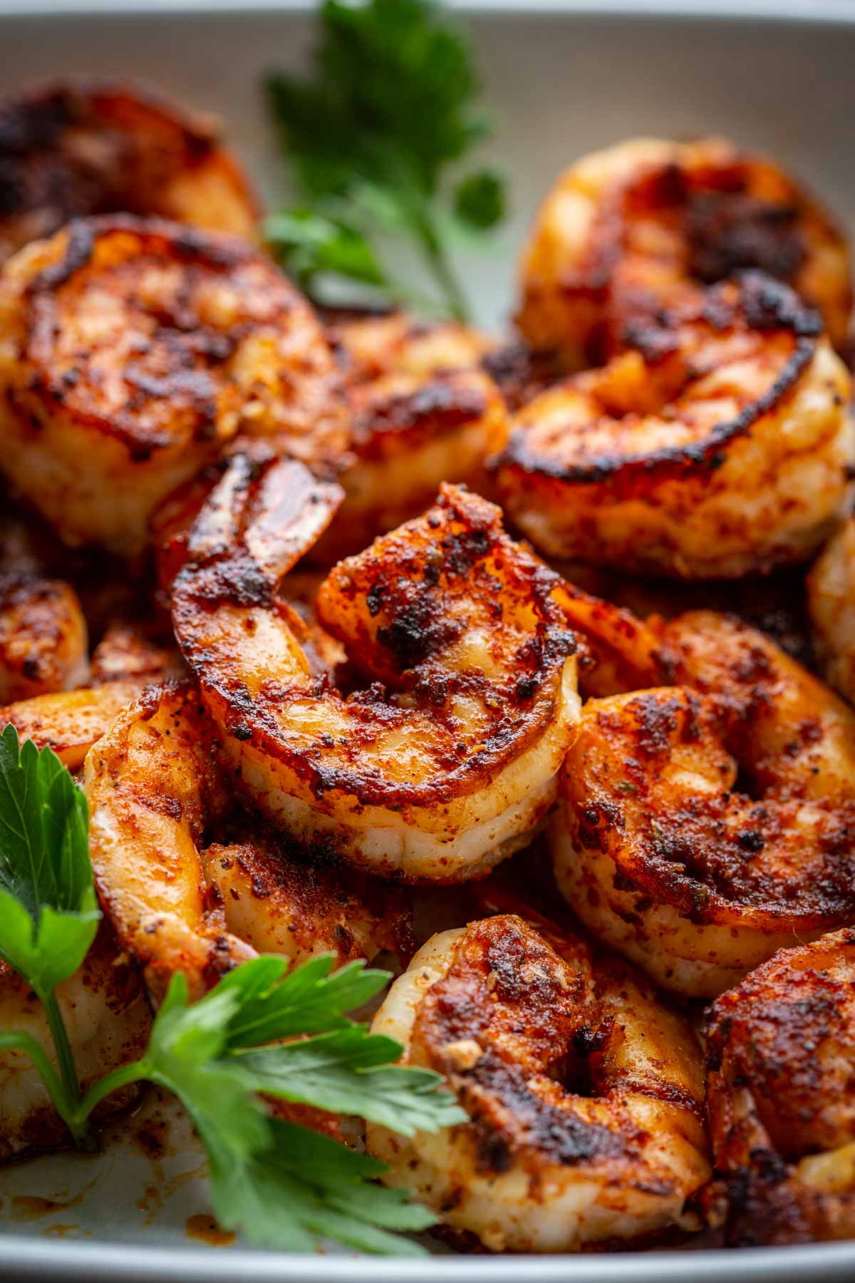 Close up of blackened shrimp with a dark spice crust next to parsley leves.