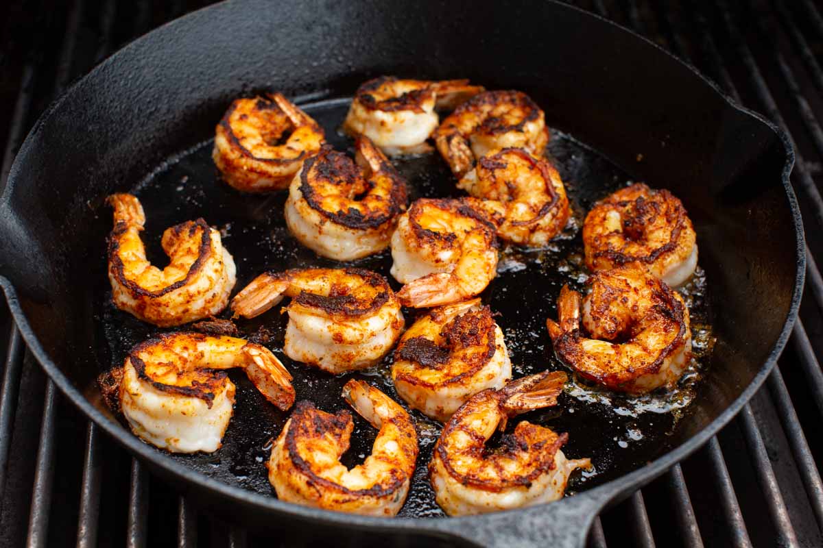 Blackened shrimp being cooked in a cast iron pan over the grill.