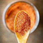 Close-up shot of a wooden spoon piled with blackening seasoning, with the filled jar blurred in the background.