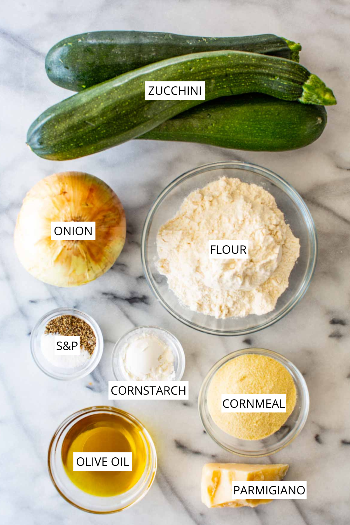 Labeled ingredients for scarpaccia laid out on a marble counter: zucchini, onion, flour, cornstarch, cornmeal, olive oil, parmigiano, and salt and pepper.