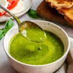 Spoon lifting basil vinaigrette out of the bowl, showing its smooth, pourable texture.