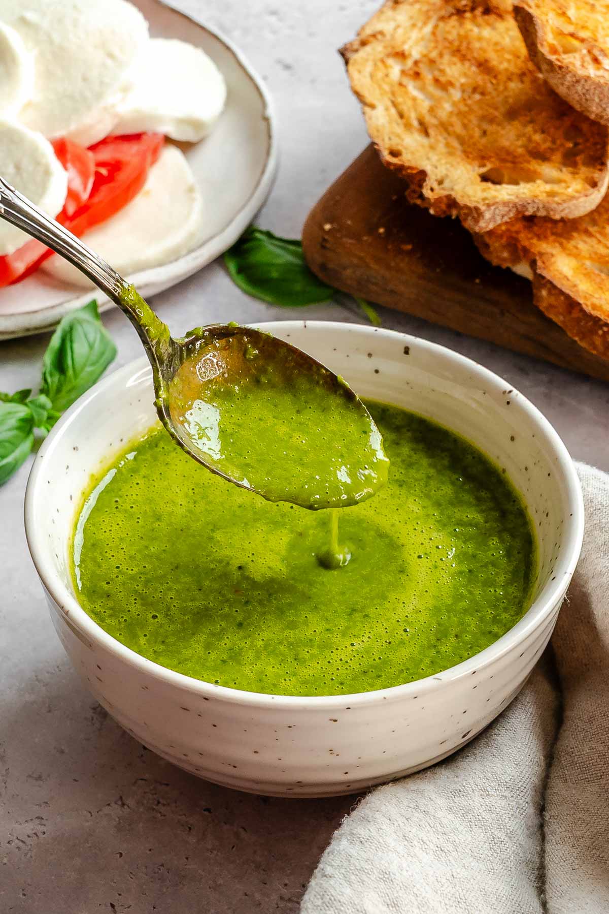 Spoon lifting basil vinaigrette out of the bowl, showing its smooth, pourable texture.