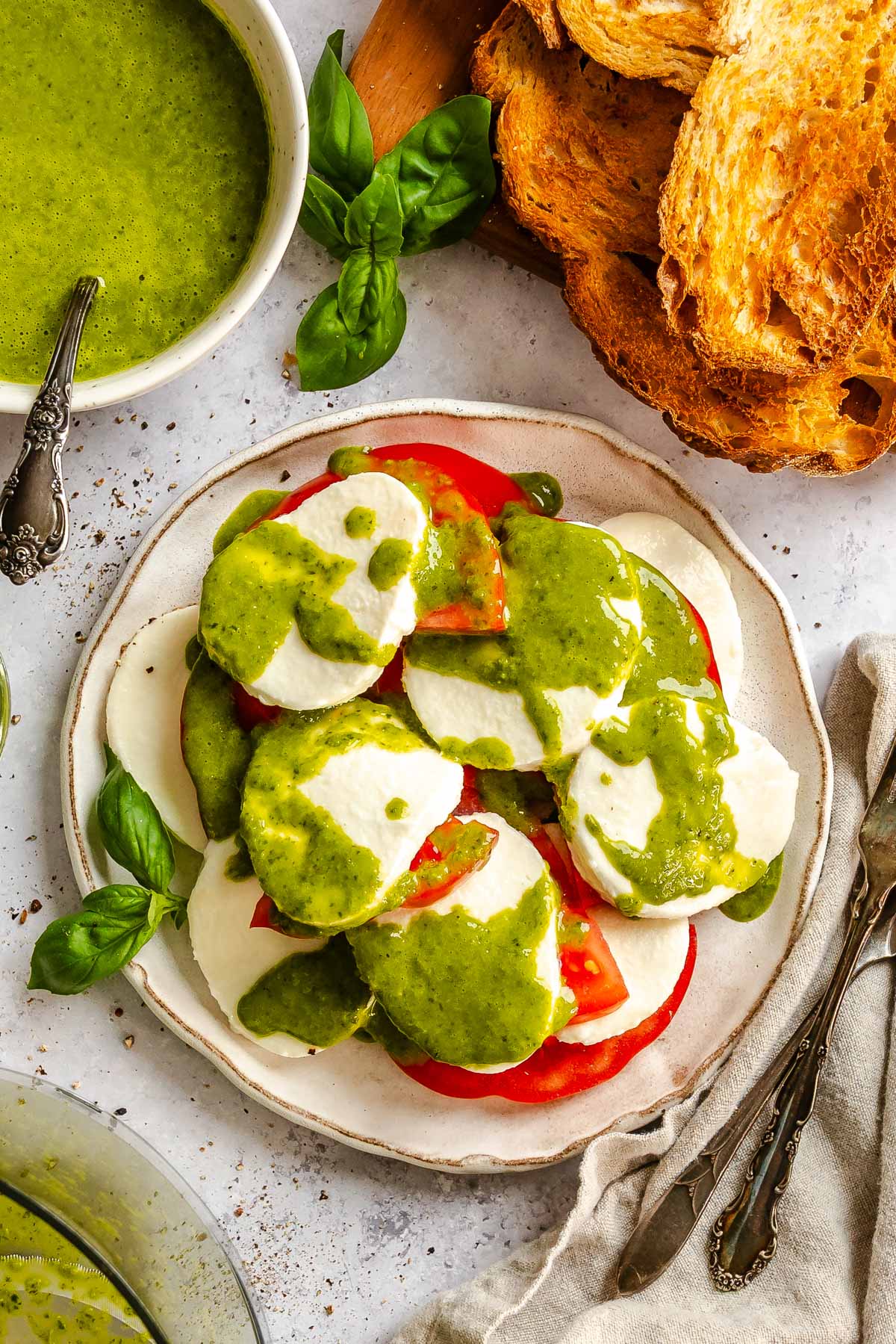 Overhead shot of a caprese salad with mozzarella and tomato slices drizzled generously with basil vinaigrette, garnished with fresh basil leaves.