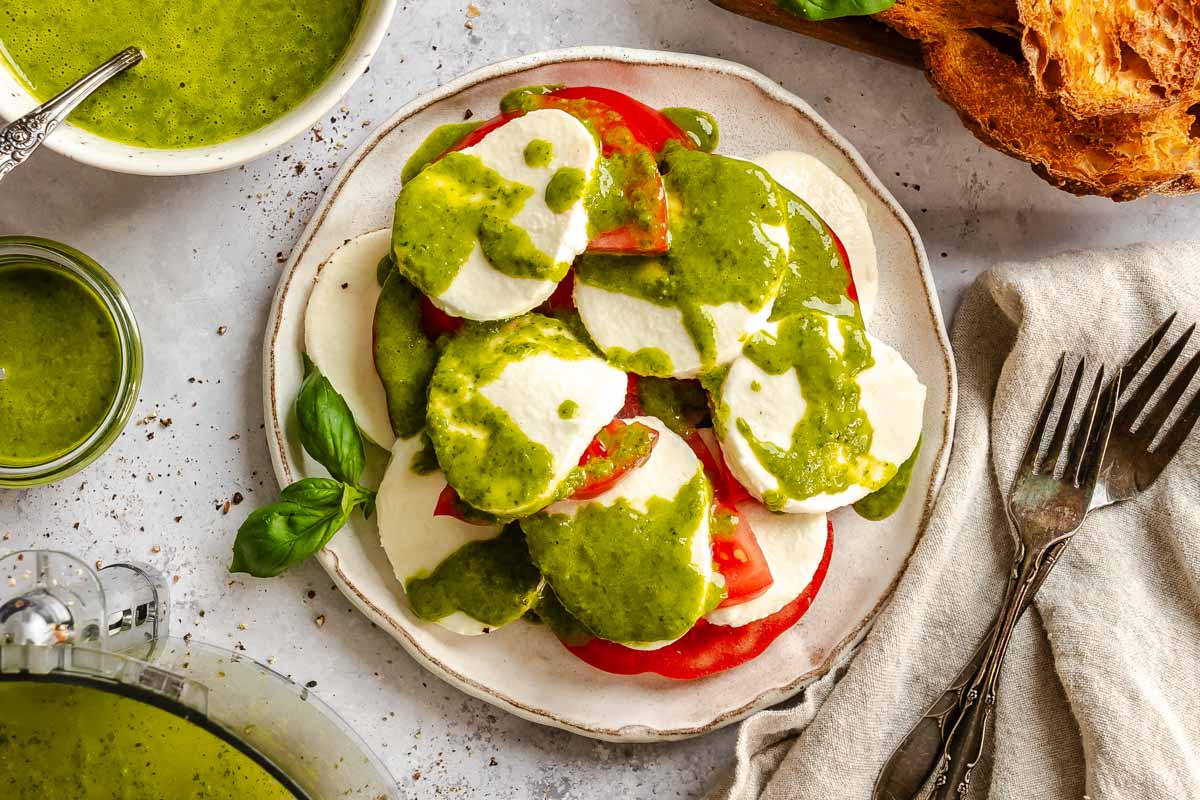 Caprese salad drizzled with basil vinaigrette, served alongside grilled bread, with extra vinaigrette and the food processor bowl in the frame.