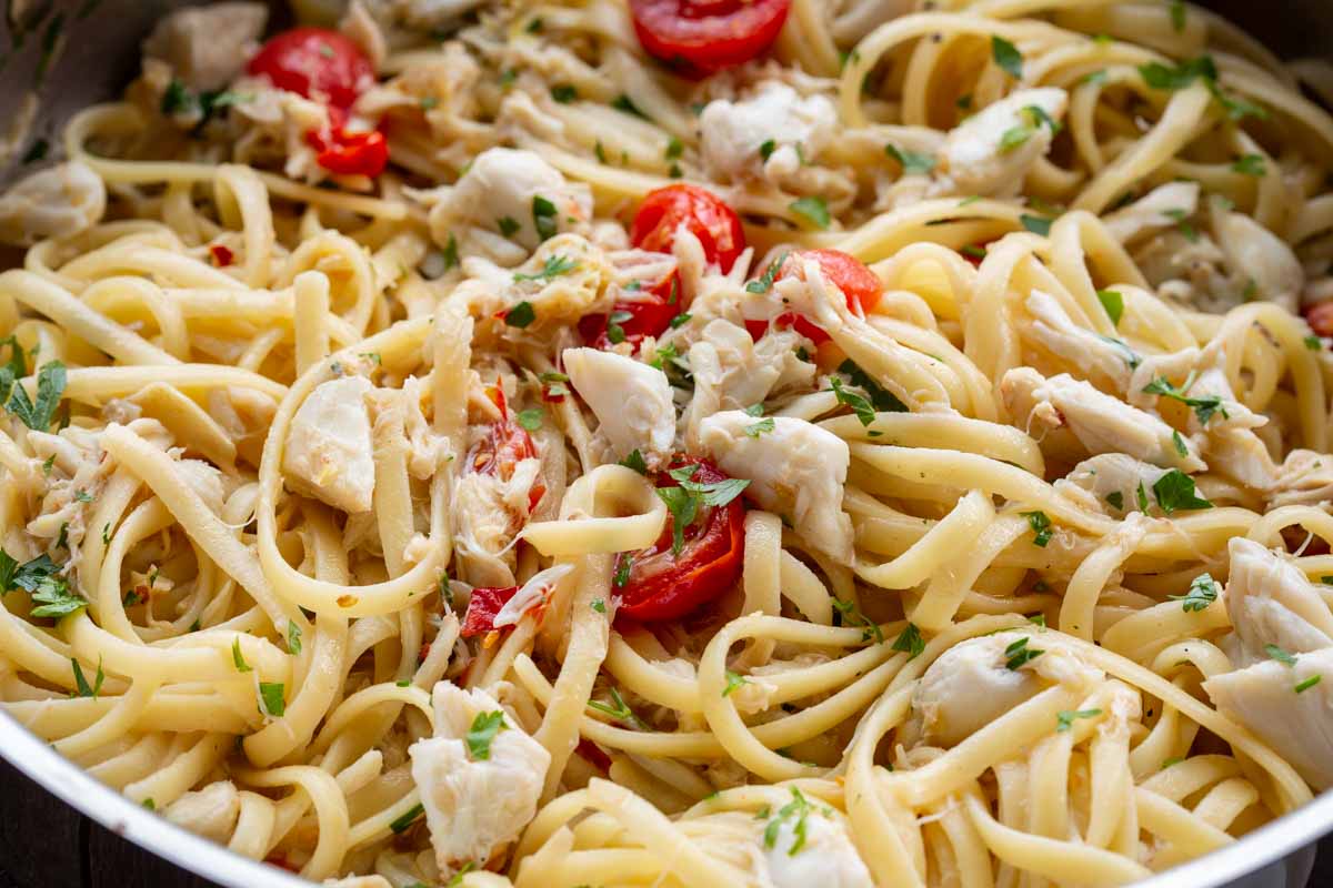 Close-up of linguine tossed with lump crab meat, halved cherry tomatoes, and chopped parsley.