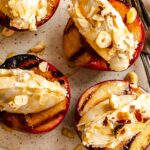 Close-up of grilled peach halves topped with creamy mascarpone and toasted hazelnuts, honey pooling on the plate beneath.
