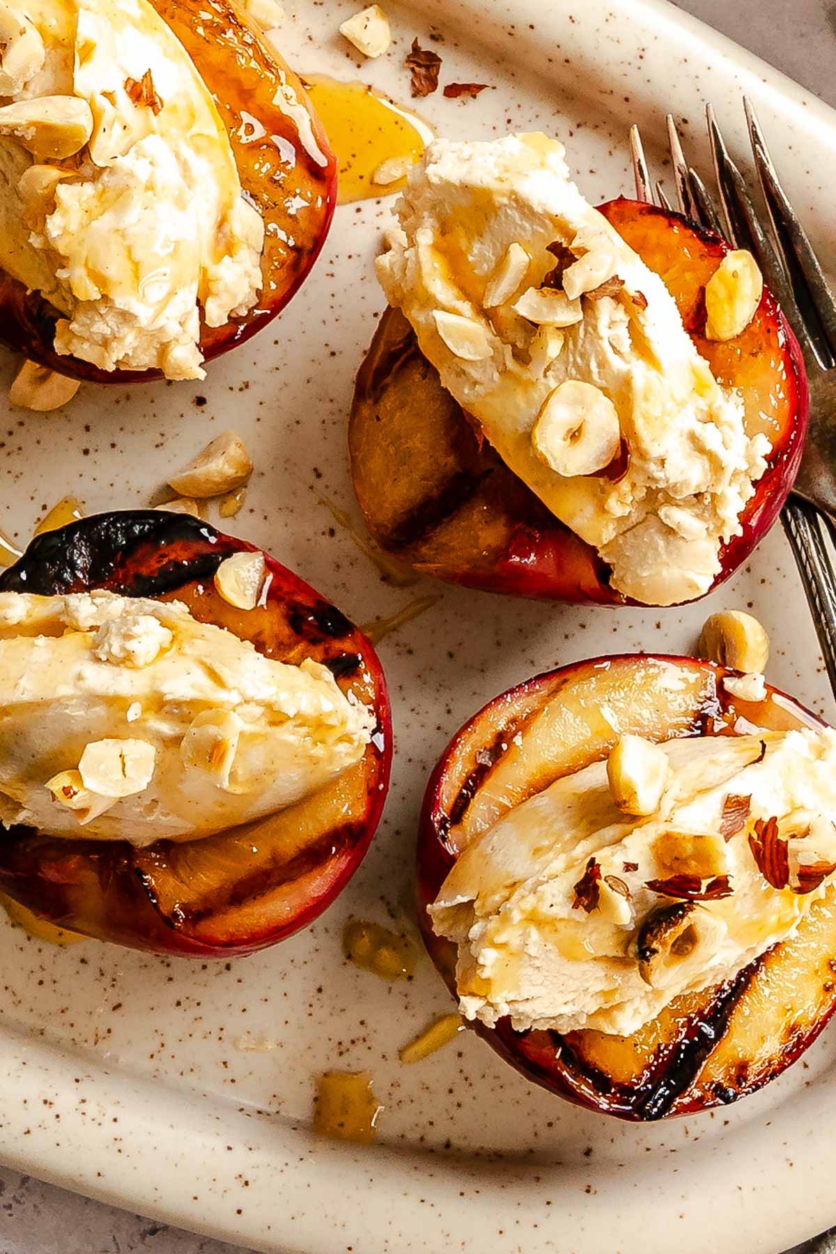 Close-up of grilled peach halves topped with creamy mascarpone and toasted hazelnuts, honey pooling on the plate beneath.