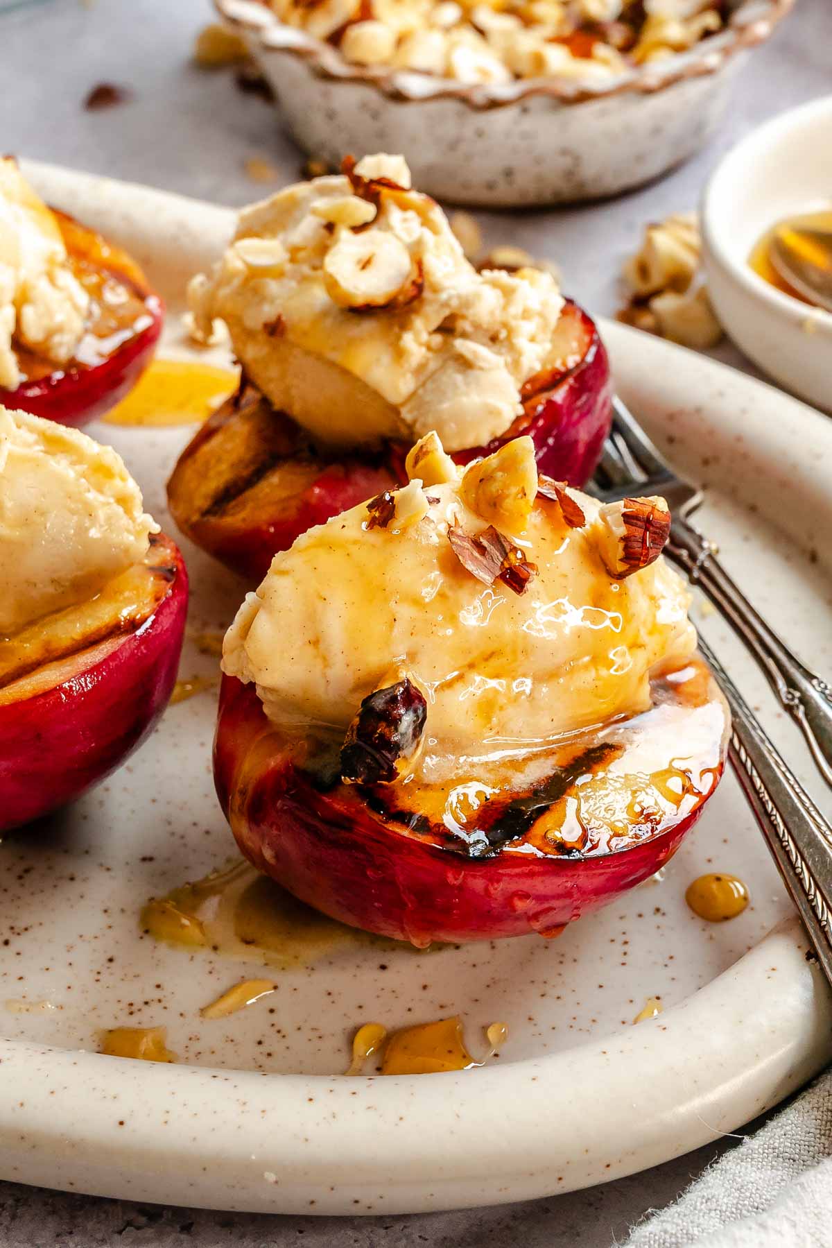 Close-up of a grilled peach half filled with mascarpone cream, drizzled with honey and topped with chopped hazelnuts, char marks visible on the peach skin.