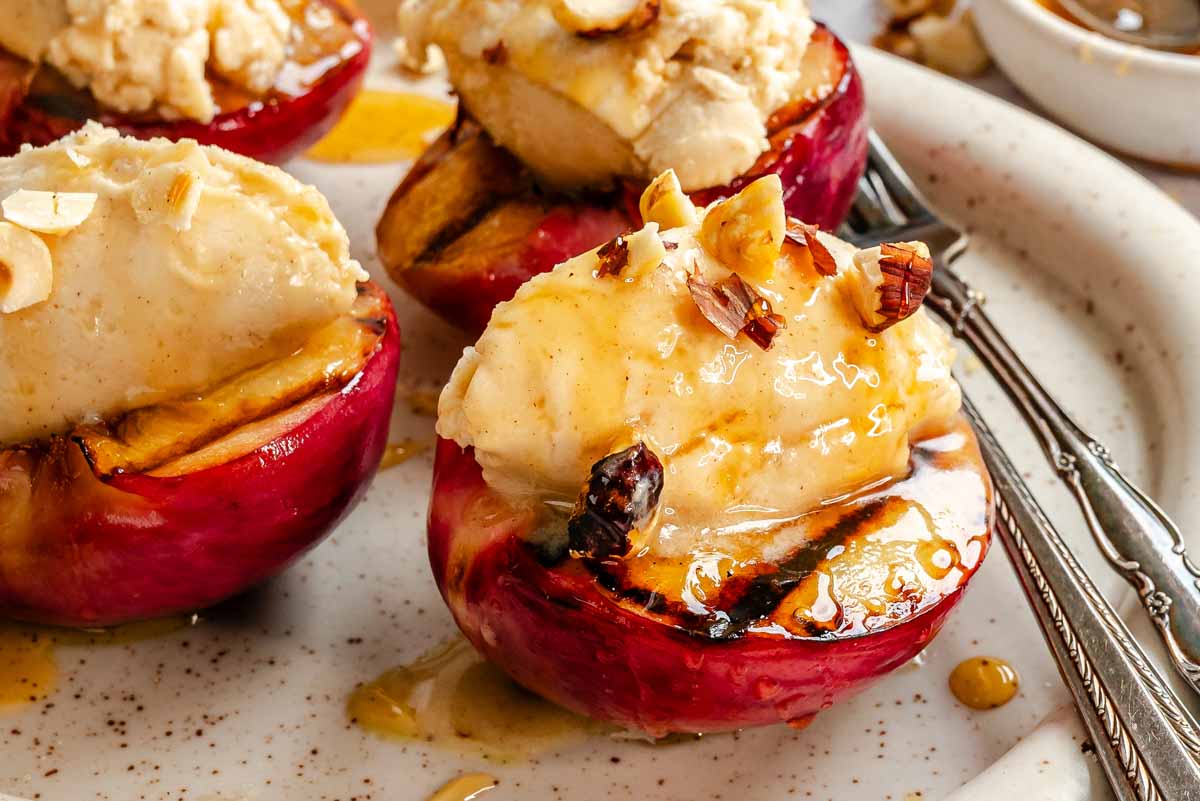 Close-up of grilled peaches topped with mascarpone and hazelnuts, honey glistening on top and pooling on the plate.