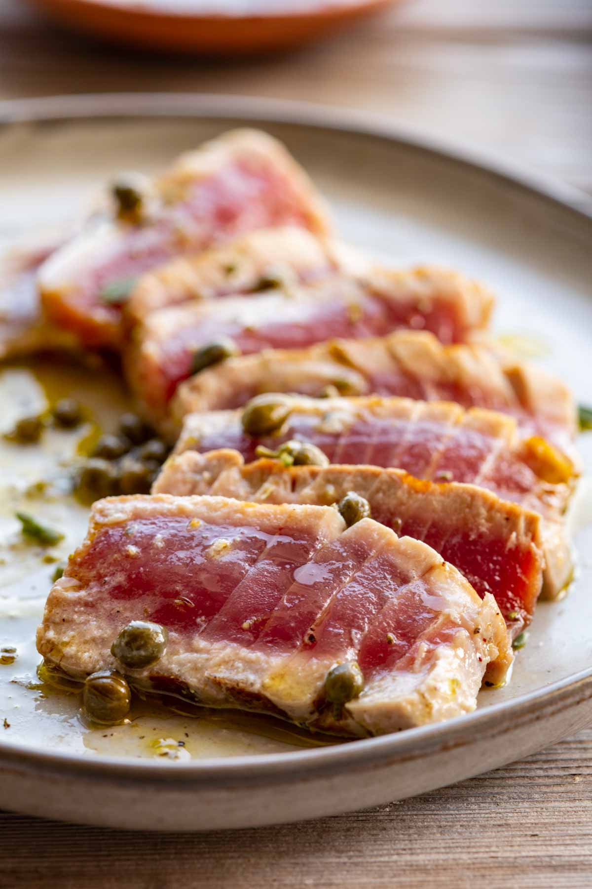 Side angle close-up of sliced grilled tuna steaks with a rosy interior, garnished with capers and glistening with vinaigrette.