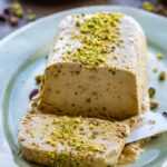 Close-up front view of the pistachio semifreddo loaf on a green platter, one slice cut and pulled forward to show the creamy interior speckled with chopped pistachios.
