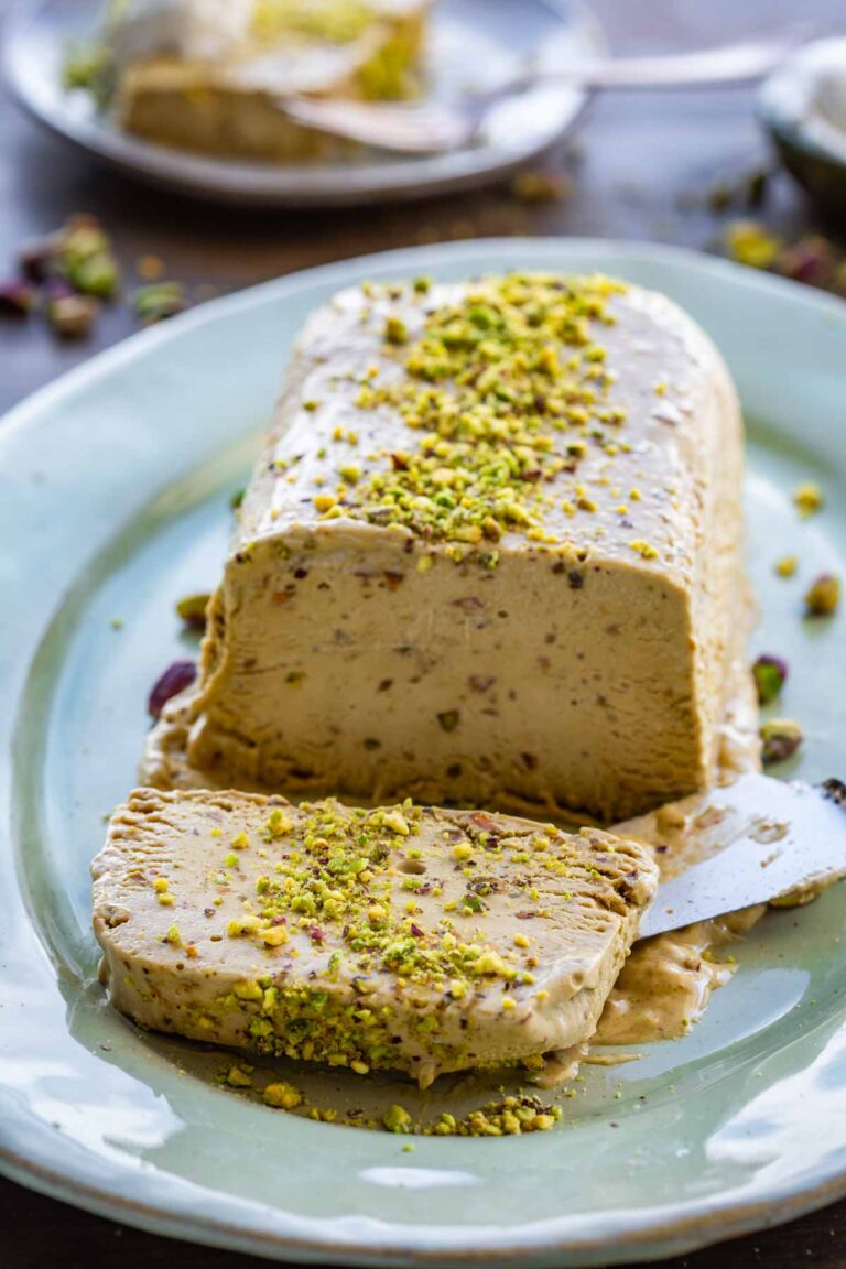 Close-up front view of the pistachio semifreddo loaf on a green platter, one slice cut and pulled forward to show the creamy interior speckled with chopped pistachios.