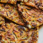 Detailed close-up of scarpaccia squares with charred zucchini ribbons and crisp golden edges, flaky texture visible where pieces overlap.