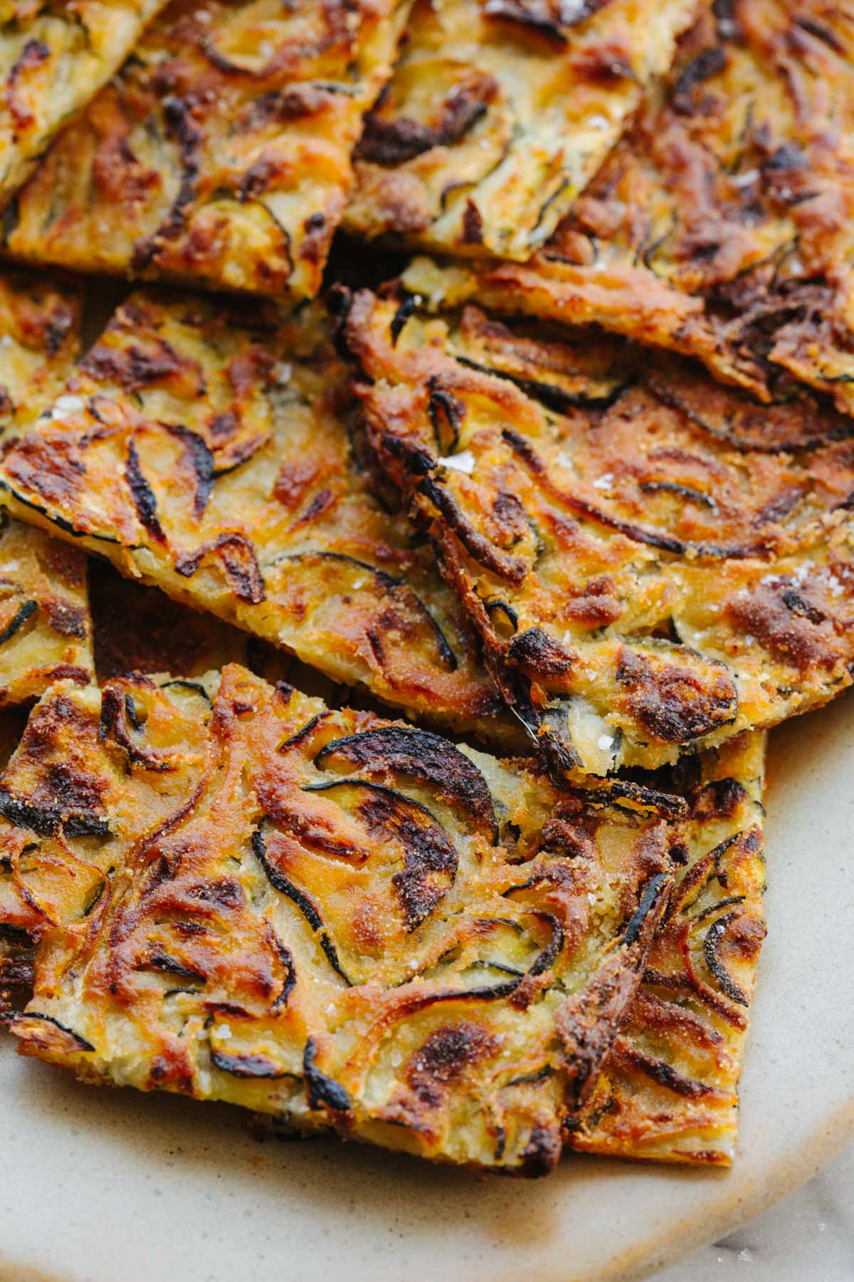 Detailed close-up of scarpaccia squares with charred zucchini ribbons and crisp golden edges, flaky texture visible where pieces overlap.