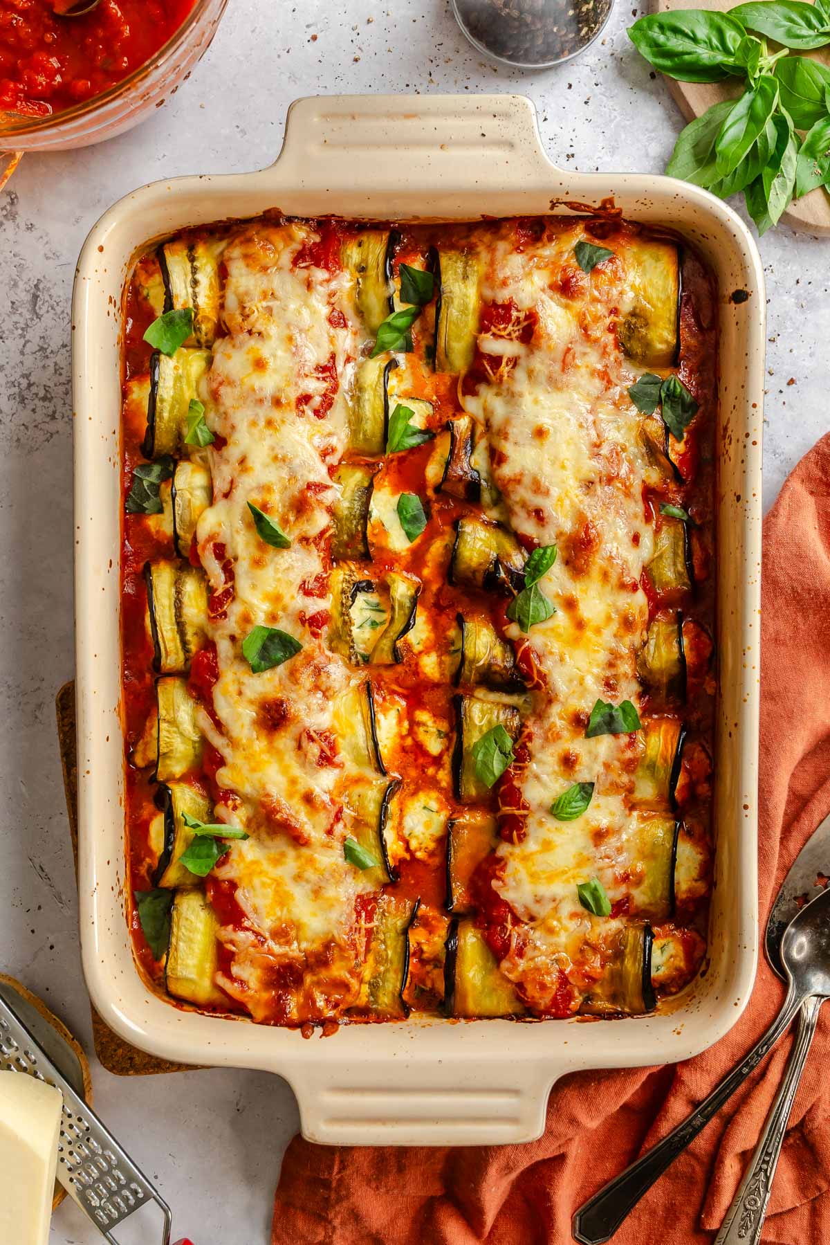 Baking dish of eggplant rollatini rolled around ricotta filling, covered in tomato sauce and bubbly melted cheese.