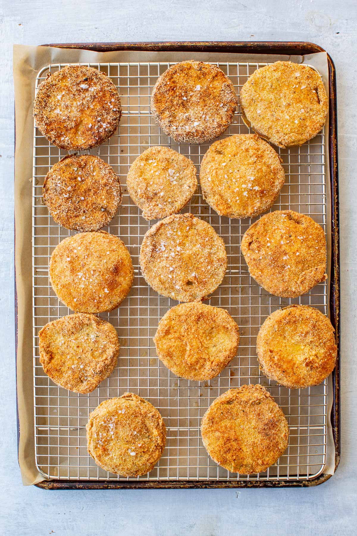 Overhead shot of thirteen golden-brown breaded fried green tomato slices on a wire rack set over a baking sheet.
