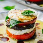 Close-up of a single eggplant caprese stack layered with mozzarella, tomato, eggplant, and basil, drizzled with oil and balsamic.