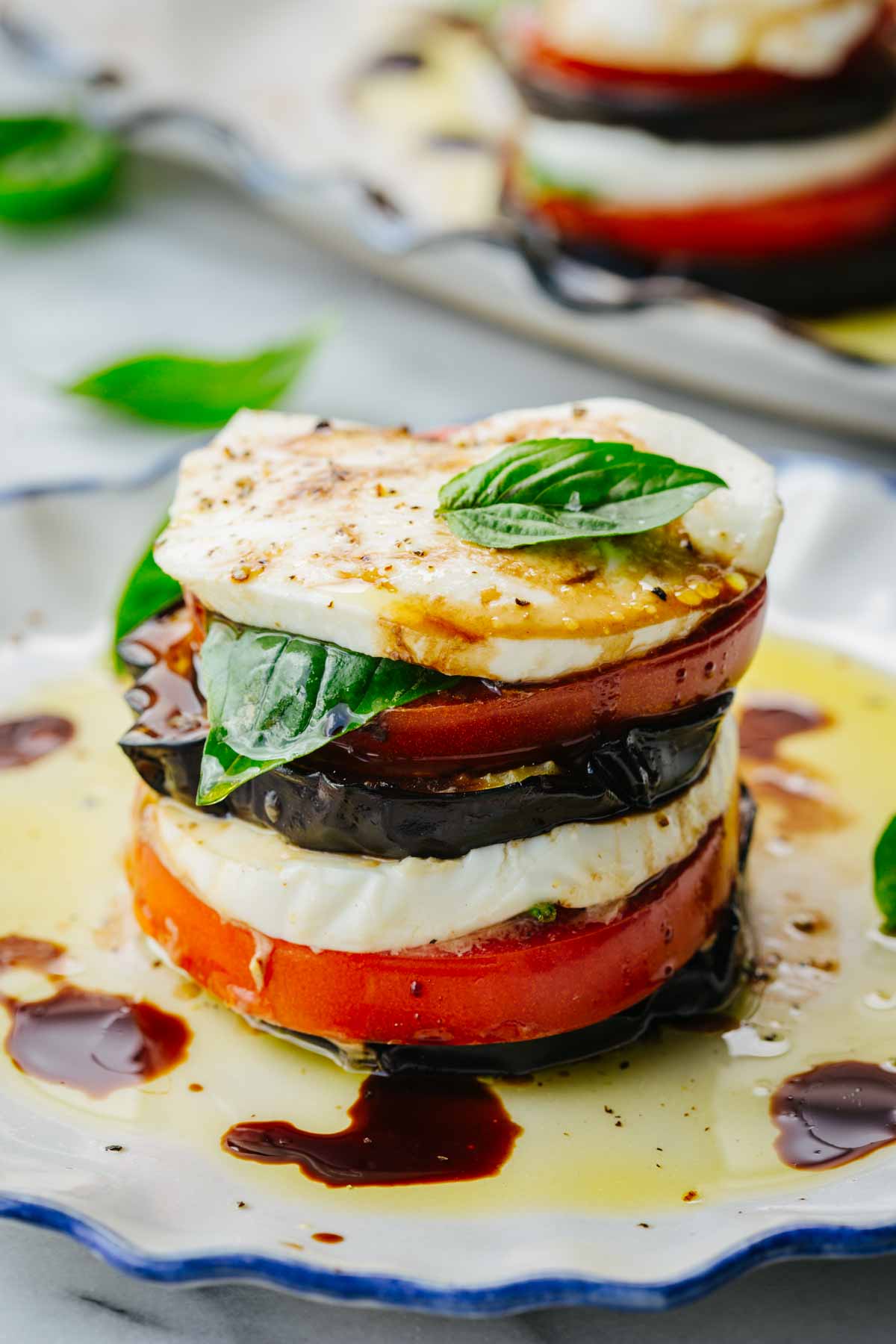Close-up of a single eggplant caprese stack layered with mozzarella, tomato, eggplant, and basil, drizzled with oil and balsamic.