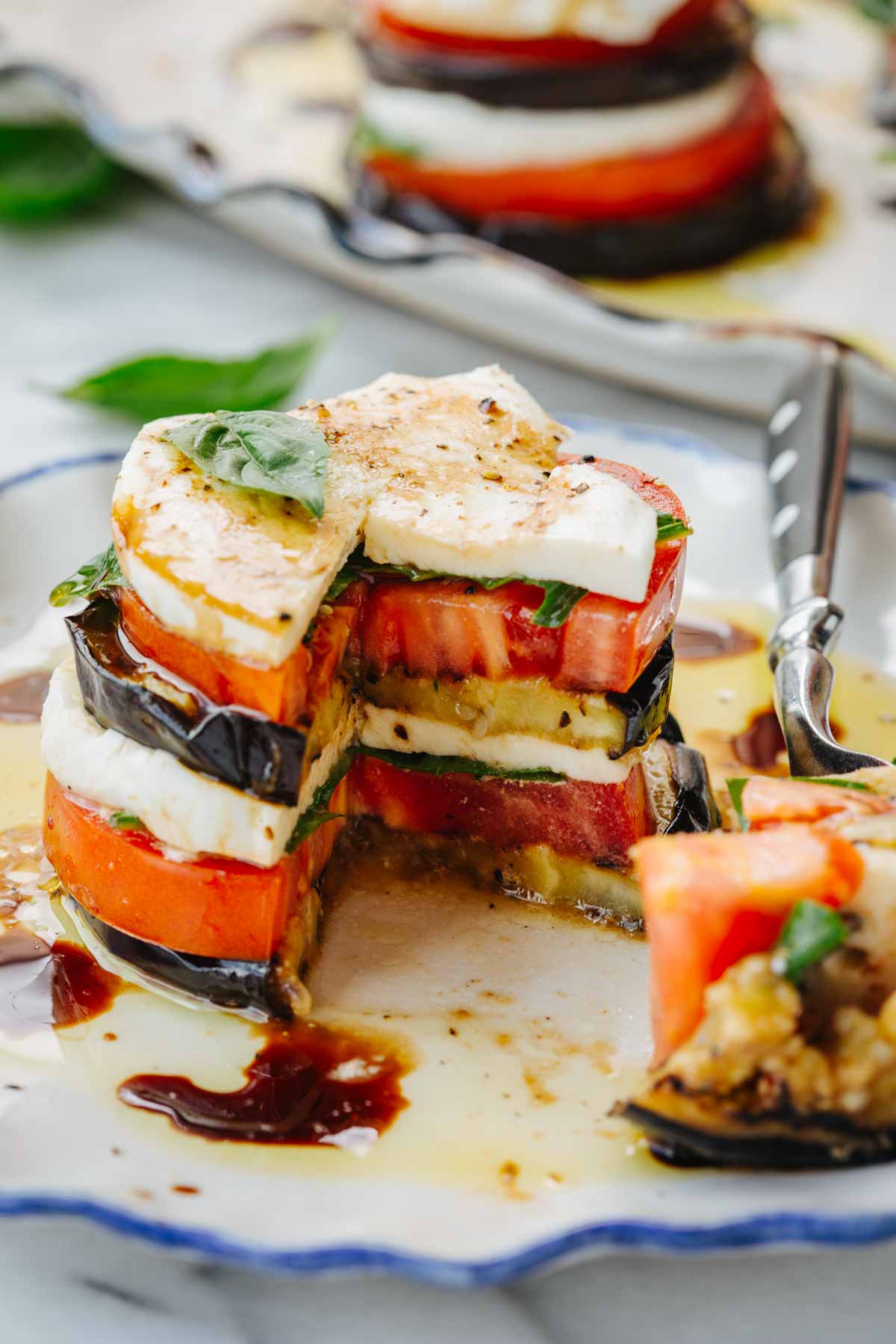 Eggplant caprese stack with a wedge cut out, revealing the layered interior, next to a fork on a decorative plate.