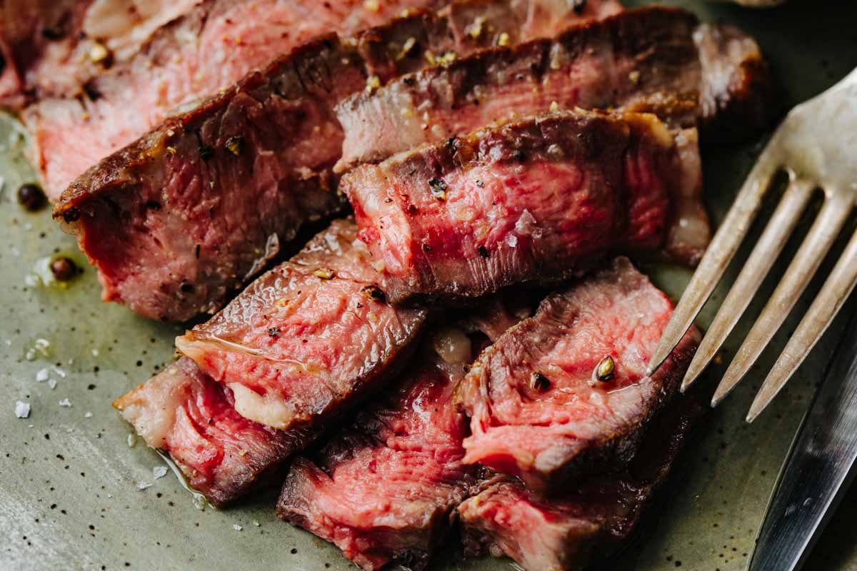 Extreme close-up of sliced medium-rare ribeye steak showing pink center and seared crust, with a fork.