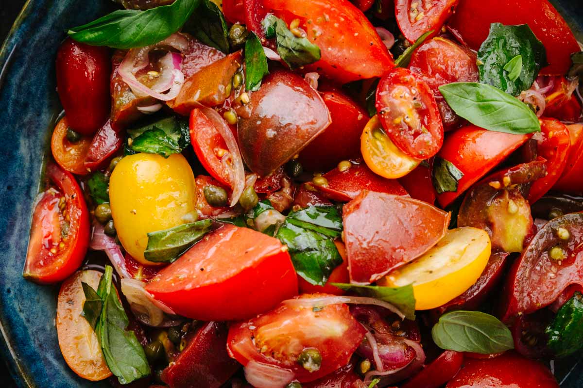 Close-up of marinated tomato pieces coated in their juices with torn basil.