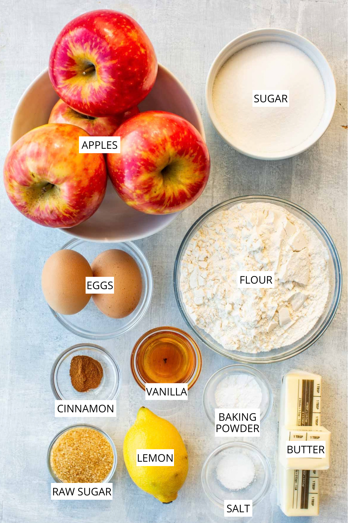 Labeled ingredients for Italian apple cake: apples, sugar, eggs, flour, cinnamon, vanilla, baking powder, raw sugar, lemon, salt, and butter.