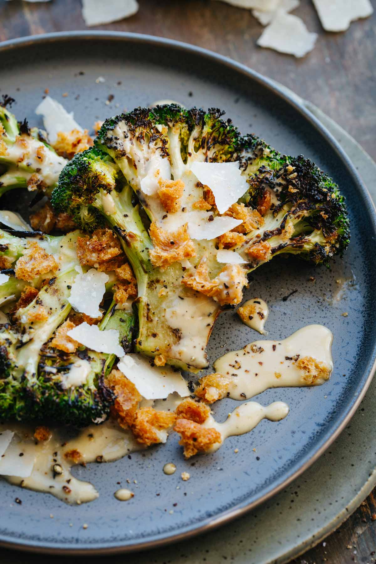 Extreme close-up of a charred broccoli floret coated in creamy Caesar dressing with crisp croutons, shaved Parmigiano, and cracked black pepper, dressing pooling on the plate.