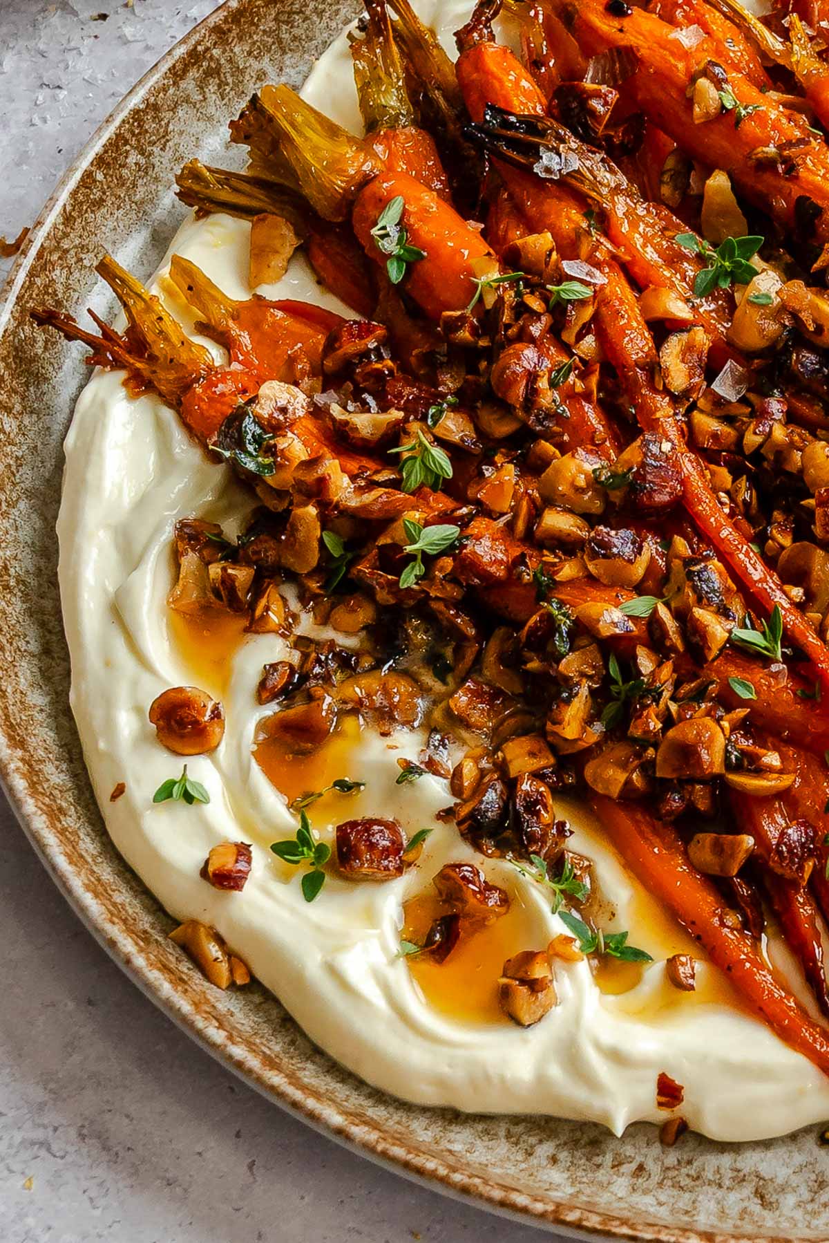 Close up of honey roasted carrots in a ceramic plate with brown butter pooled over creamy whipped ricotta.