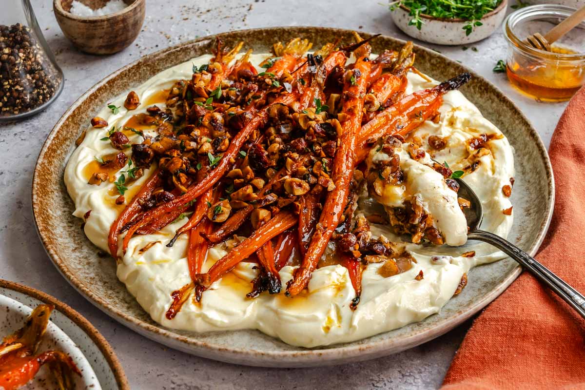 Side view of honey roasted carrots in a ceramic plate with a serving spoon.