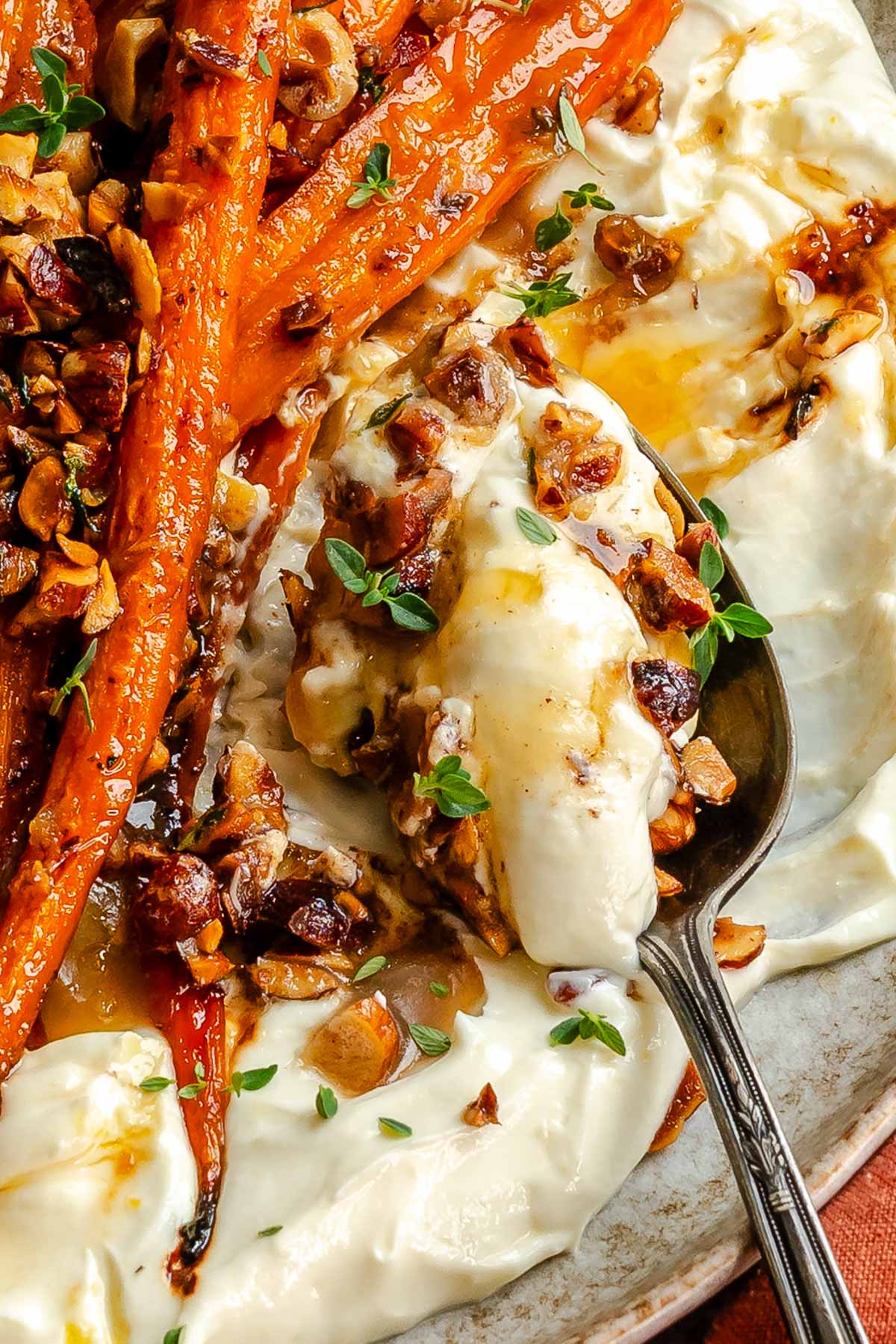 Close up of a spoon holding creamy whipped ricotta next to honey roasted carrots.