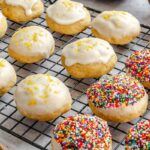 Lemon ricotta cookies cooling on a wire rack, some topped with lemon glaze and fresh lemon zest, others coated in rainbow nonpareil sprinkles.
