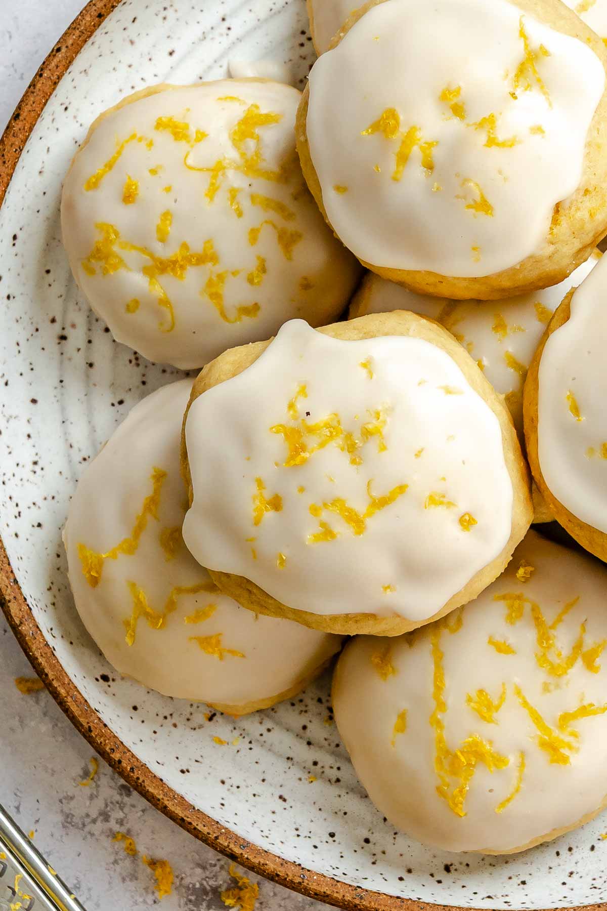 Overhead close-up of lemon ricotta cookies with a thick lemon glaze and scattered lemon zest on top.