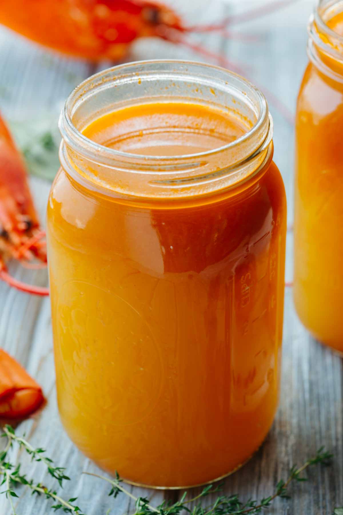 Overhead close-up of a mason jar of lobster stock, garnished with sprigs of fresh thyme and parsley nearby.