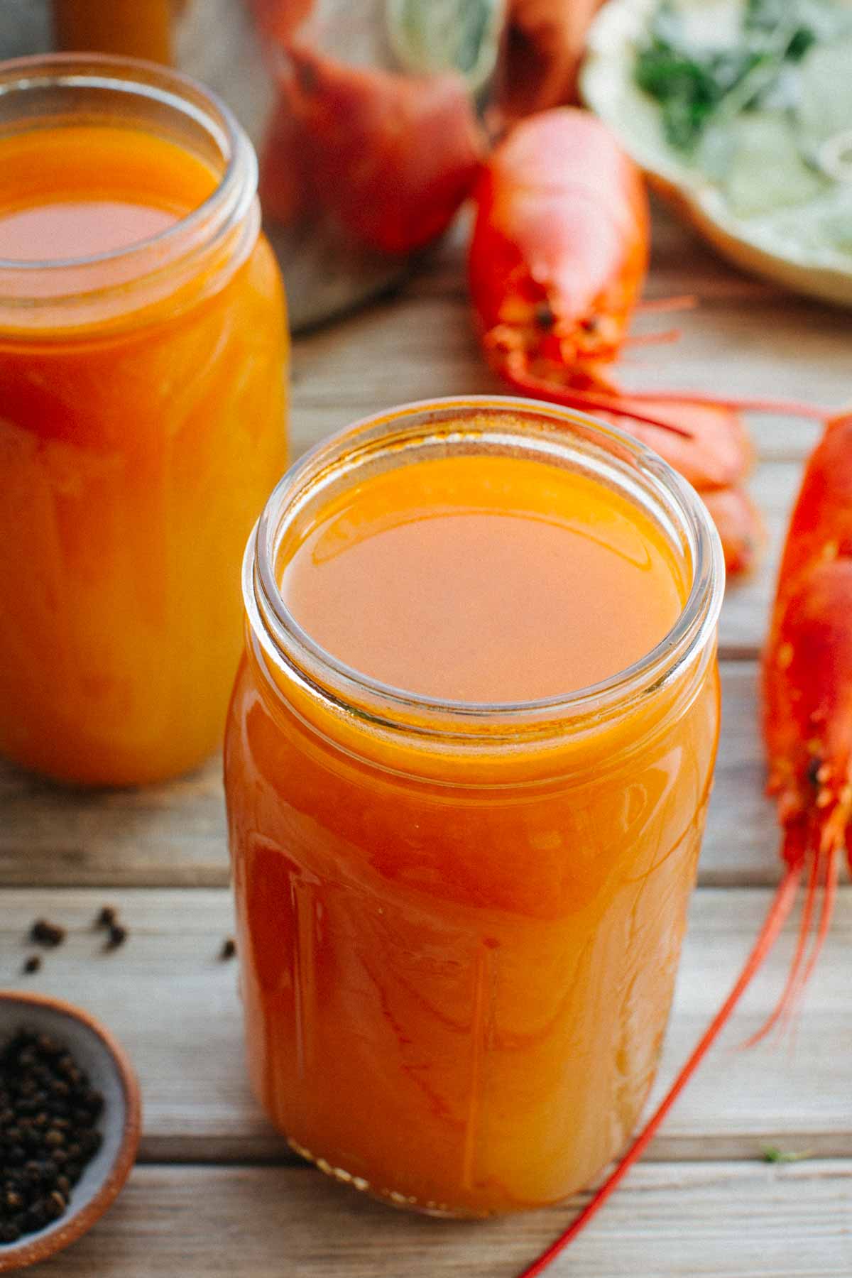 Close-up of mason jars filled with strained lobster stock, with a lobster shell and stockpot visible in the background.