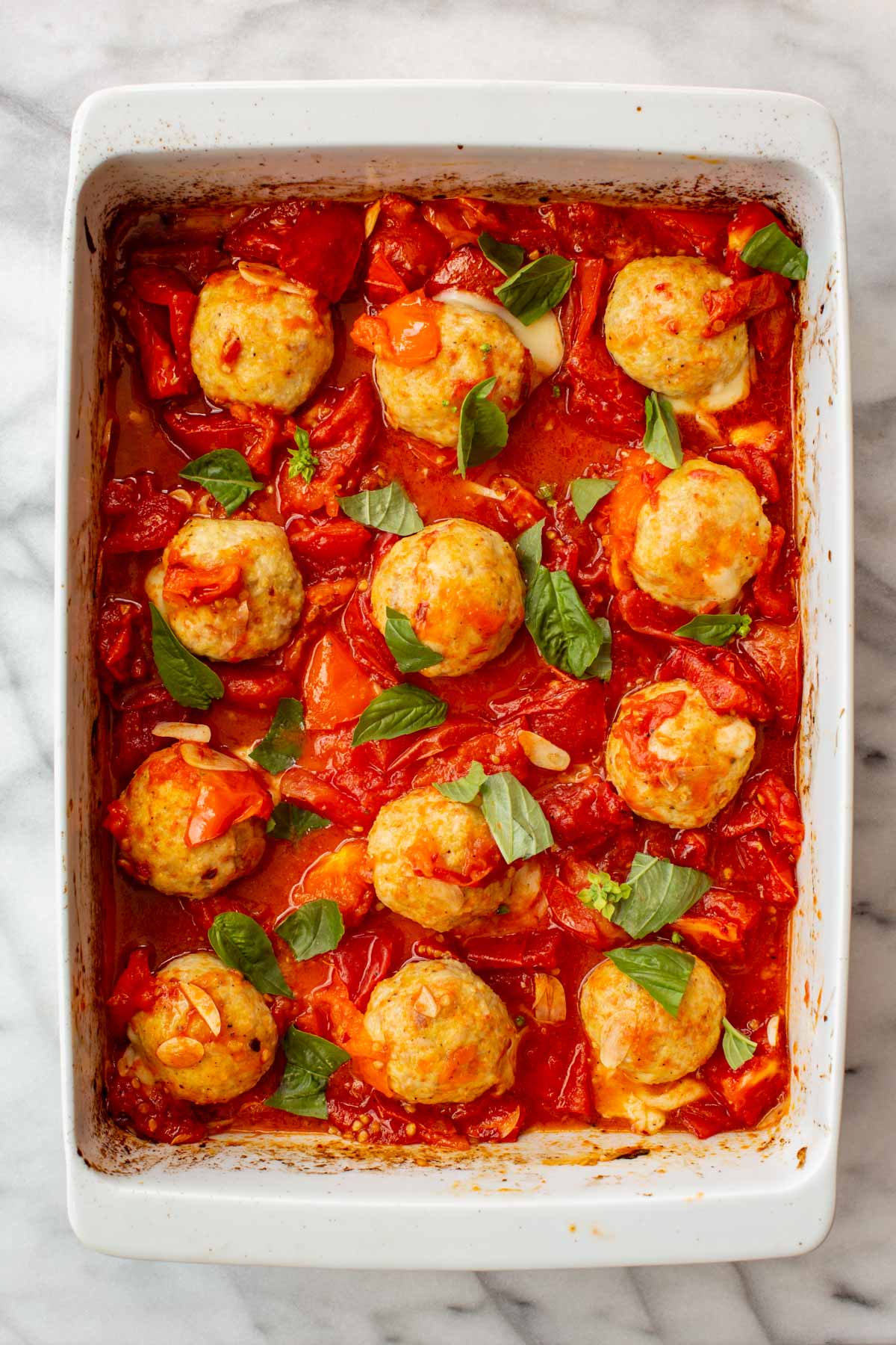 Baked chicken meatballs in roasted tomato sauce topped with torn fresh basil leaves.