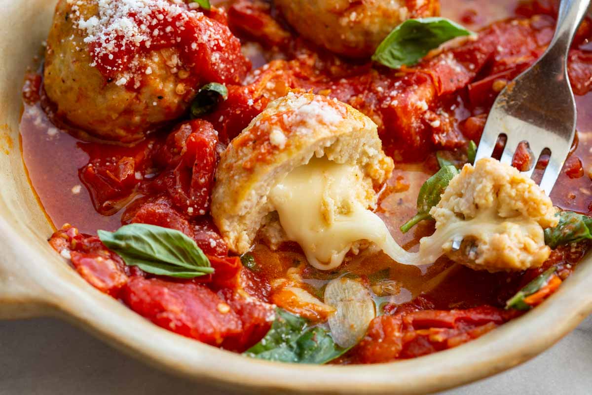 Close-up of a stuffed chicken meatball with melted mozzarella oozing out of the center next to a fork.