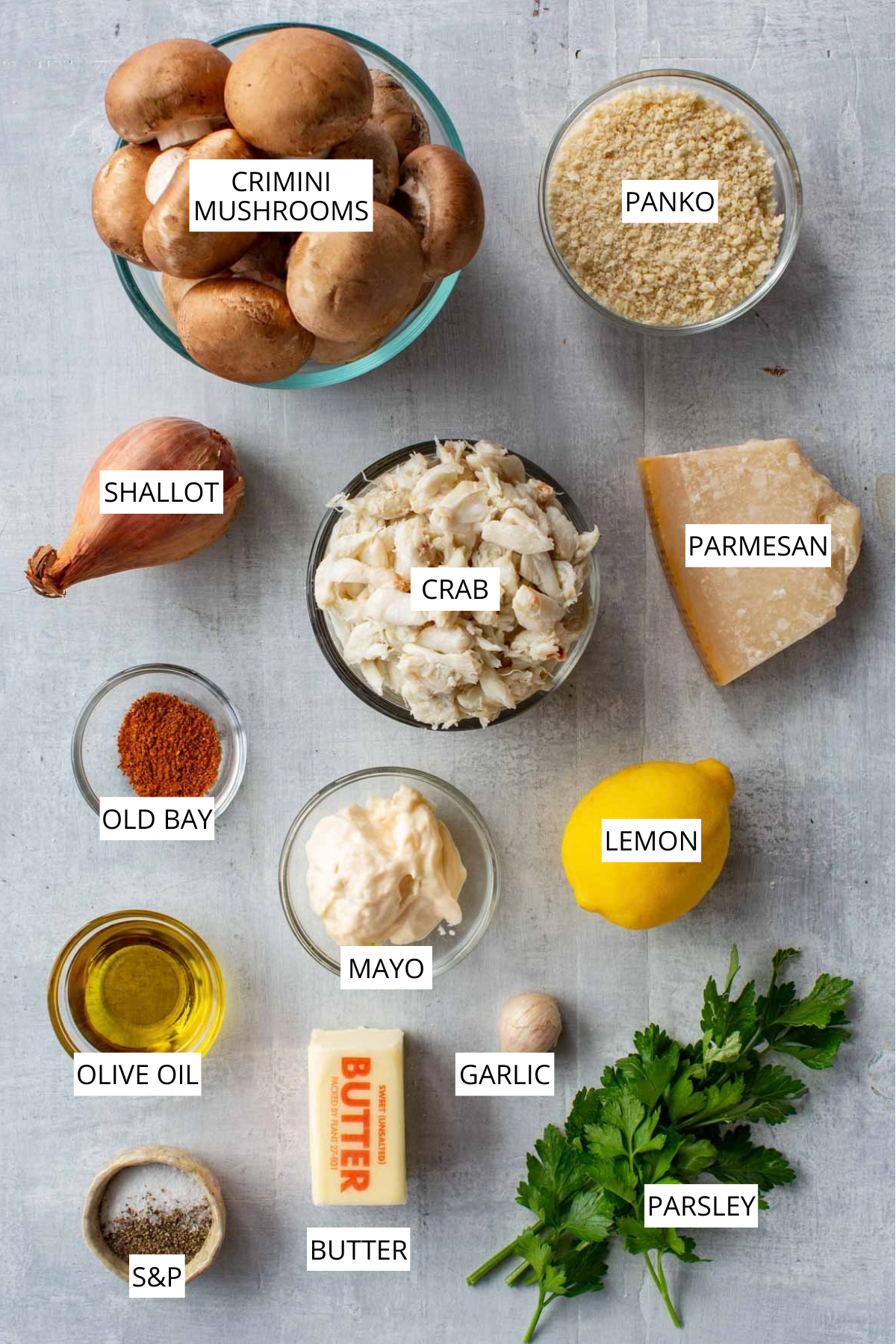 Labeled ingredients for crab stuffed mushrooms: crimini mushrooms, panko, shallot, crab, parmesan, Old Bay, mayo, lemon, olive oil, garlic, butter, parsley, and salt and pepper.