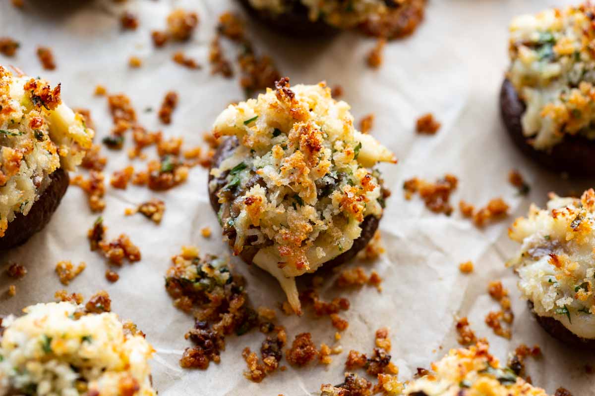 Close-up of a crab stuffed mushroom with a crisp golden panko topping, flecks of parsley, and visible lumps of crab on parchment paper.