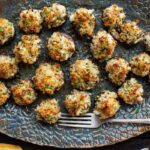 Platter of golden, crispy crab stuffed mushrooms on a blue ceramic plate with a vintage silver fork.